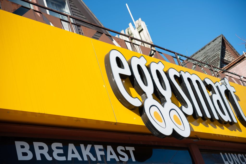 The yellow and white exterior sign for Eggsmart, a breakfast restaurant in Toronto, Canada.