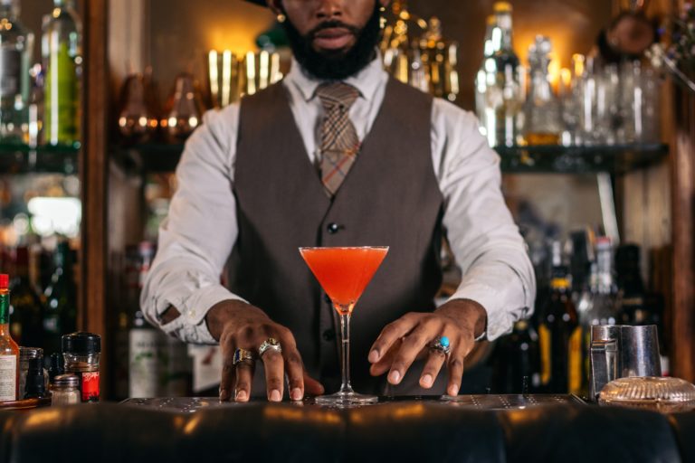 A bartender serving a bright orange cocktail in a martini glass.