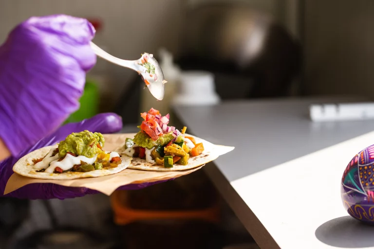 A food vendor prepares two tacos by adding salsa.