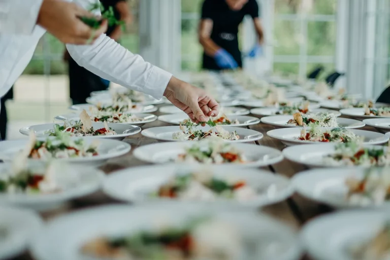 A catering server garnishes a dish at a wedding reception.