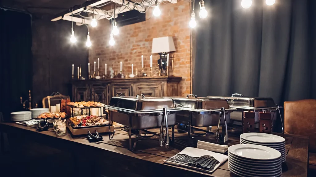 A table at a catered event covered in platters of appetizers and chafing dishes.