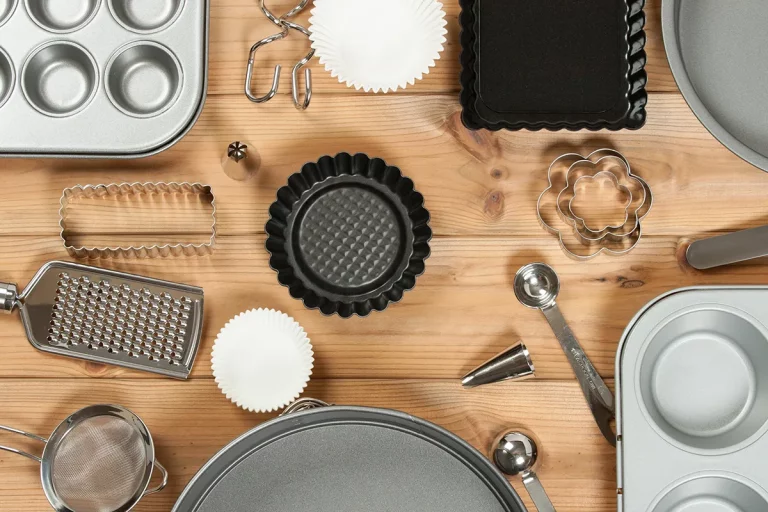 Various baking supplies laid out flat on a wooden countertop, including cookie cutters and muffin pans.