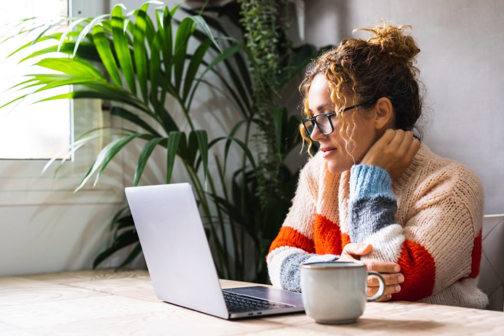 Woman sitting by a computer with a cup of coffee next to her.