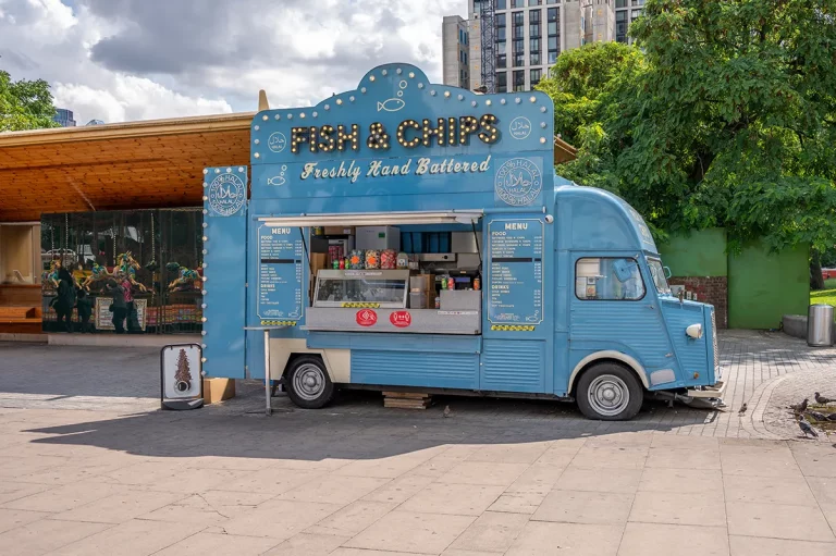 A sky blue food truck selling fish and chips parked along the River Thames in London.