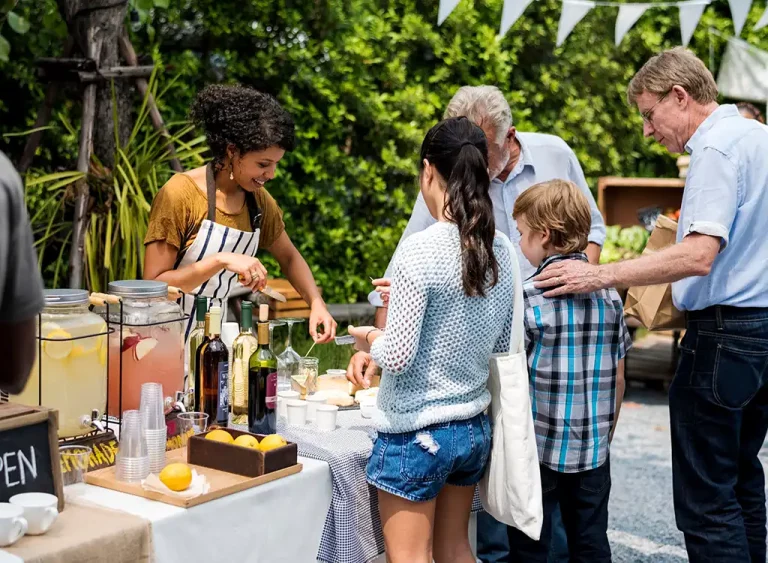 Group of customers at a farmers market waiting at a lemonade stand.