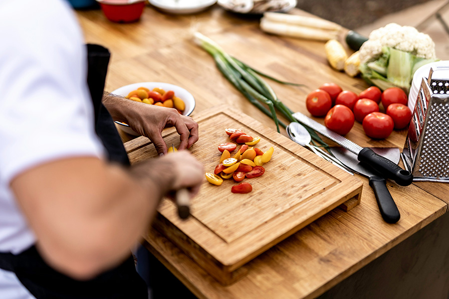 A personal chef chops cherry tomatoes on a wooden cutting board.