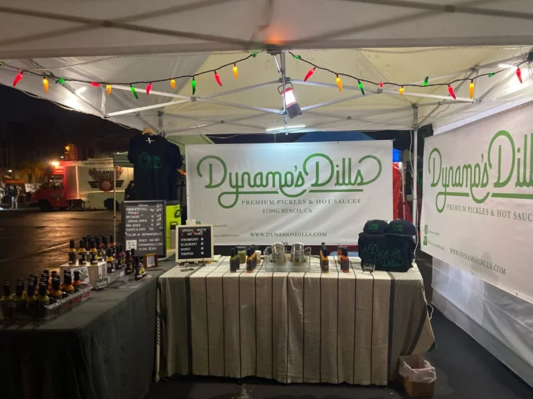 The Dynamo's Dills booth under a canopy with hot sauces and other products displayed on their tables.
