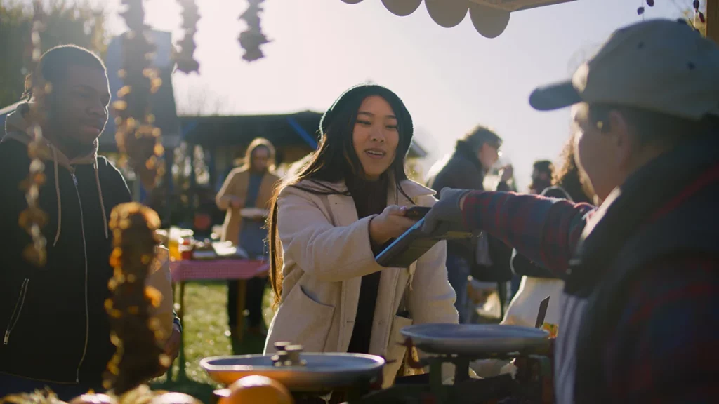 A farmers market customer uses a smartphone to pay for goods at a booth.