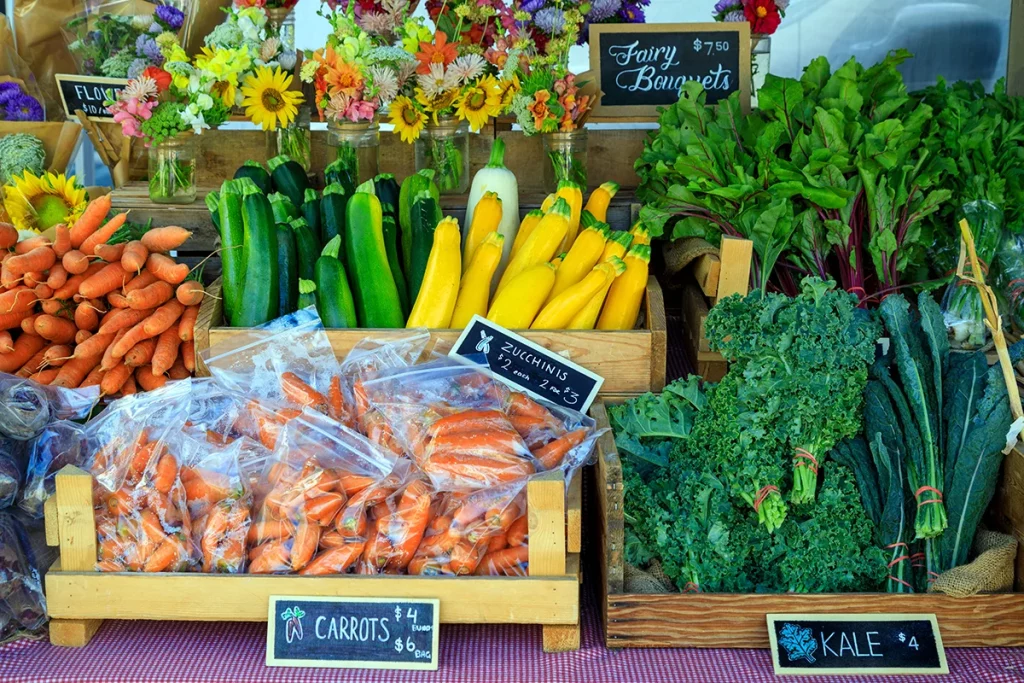 A display of fresh produce at a farmers market booth with chalkboard signage.