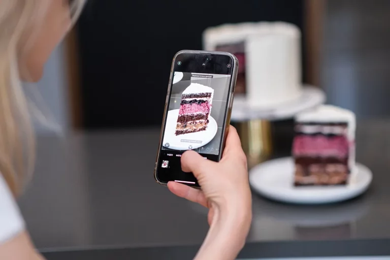 A woman taking a picture of a multi-layered slice of cake with a smartphone.