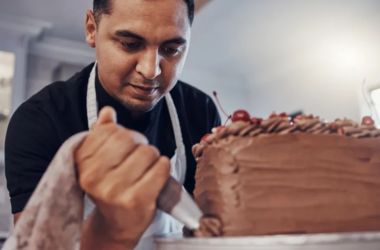 A home baker pipes chocolate frosting onto a cake.