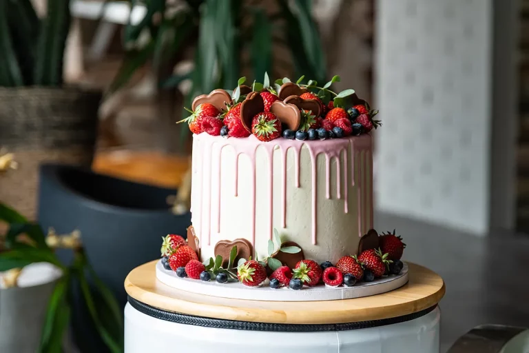 A professionally made cake with a dripping pink glaze, topped with fresh berries and chocolates.