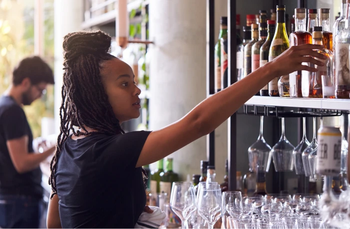 A woman grabbing a liquor bottle from a shelf.