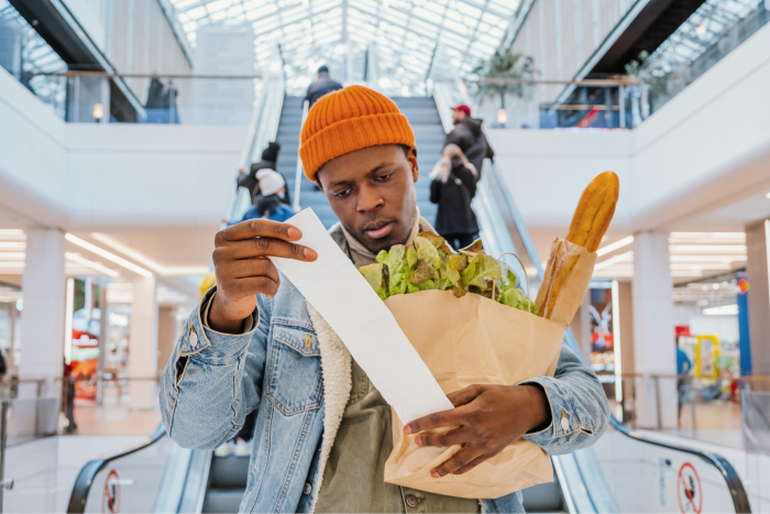 A man holding a bag of groceries and reading a receipt.